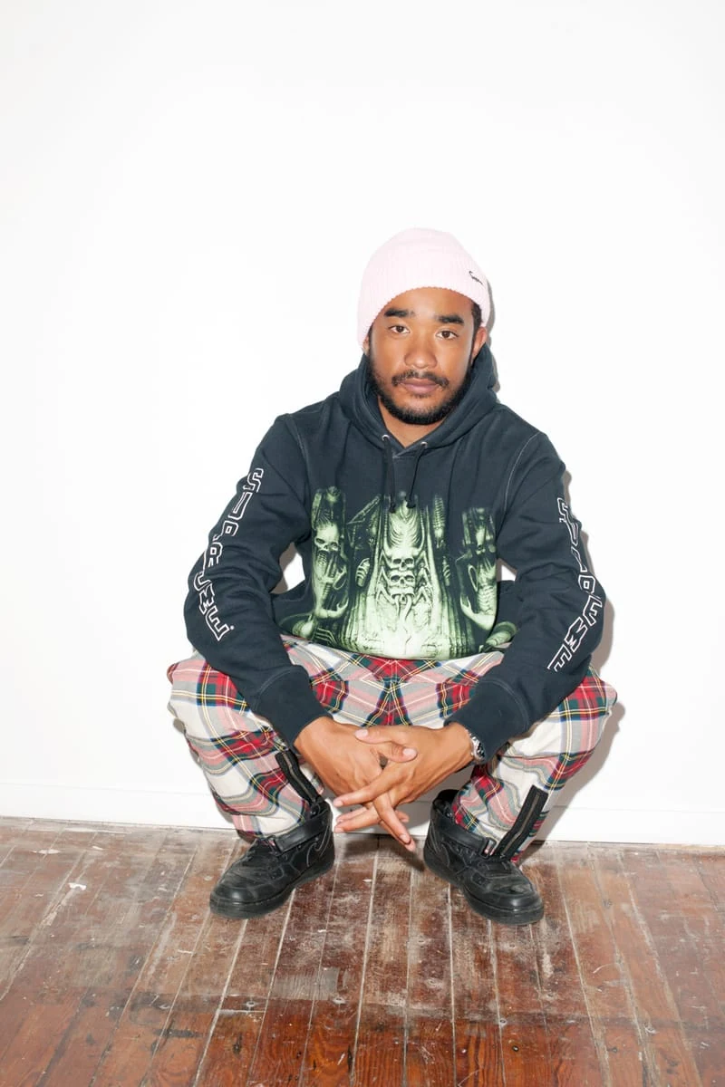 Lucien Smith crouching in a black graphic hoodie, plaid trousers and pink cap for the SENSE Supreme Fall/Winter 2014 editorial